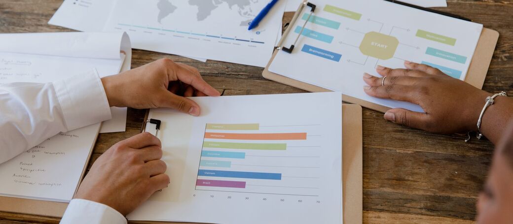 Two people at a desk reviewing printed bar charts and business reports